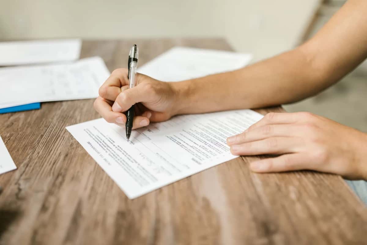 Personne remplissant un formulaire administratif au stylo sur un bureau en bois