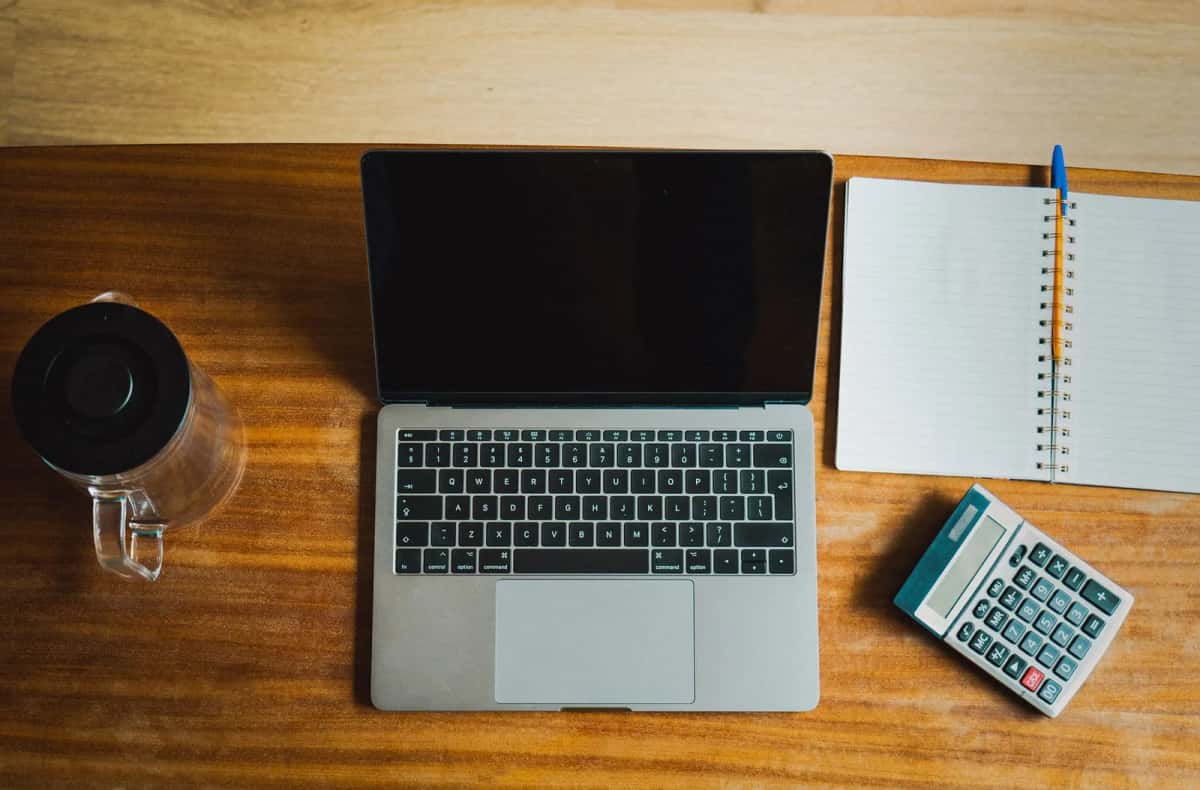 Ordinateur portable, calculatrice et carnet posés sur un bureau en bois