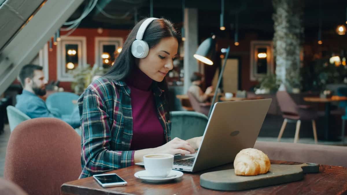 Une femme avec un casque travaille sur un ordinateur portable dans un café