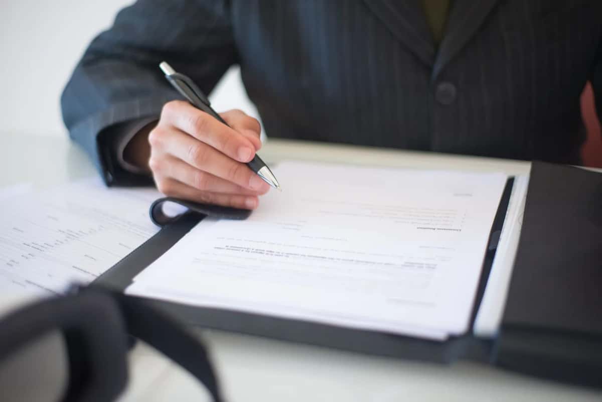 Une personne en costume signe un document posé dans un classeur sur un bureau