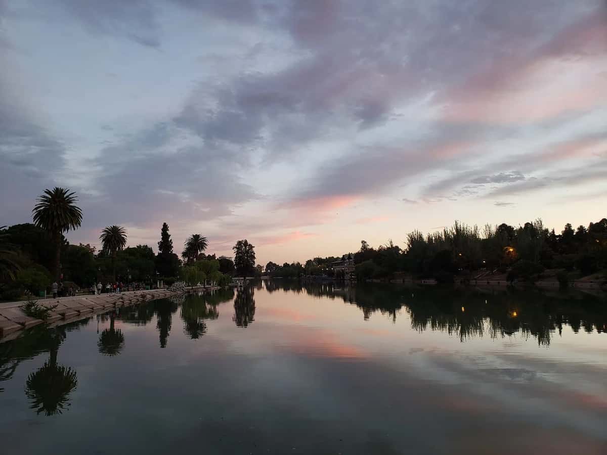 Le lac du parc général San Martín à Mendoza au crépuscule, avec des palmiers et des promeneurs sur la rive